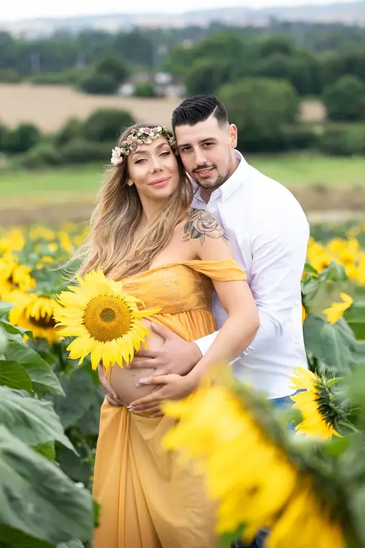 Expectant couple standing together among sunflowers