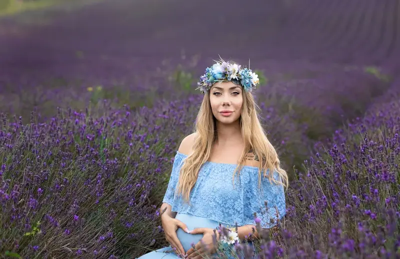 Expectant mother in a blue lace dress and flower crown sitting in a lavender field