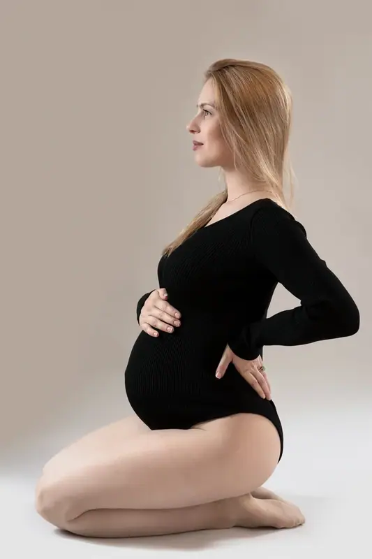 Expectant mother in a black bodysuit kneeling in profile, studio portrait