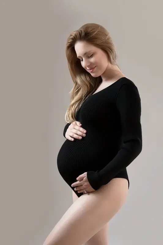 Expectant mother in a black bodysuit standing in profile, studio portrait