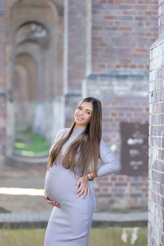 Expectant mother in a lilac dress standing in an old brick archway
