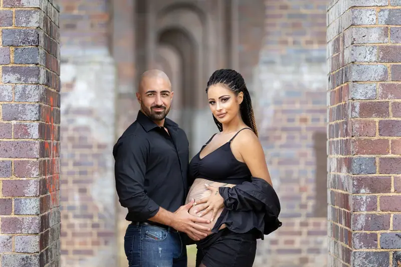 Expectant couple in black standing in a brick archway