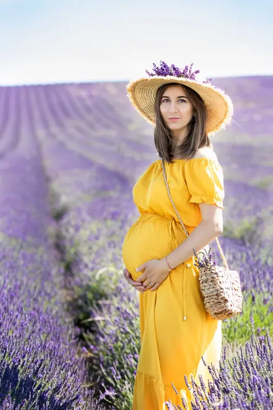 Expectant mother in a yellow dress and hat standing in a lavender field