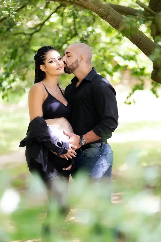 Expectant couple embracing beneath a tree in a park