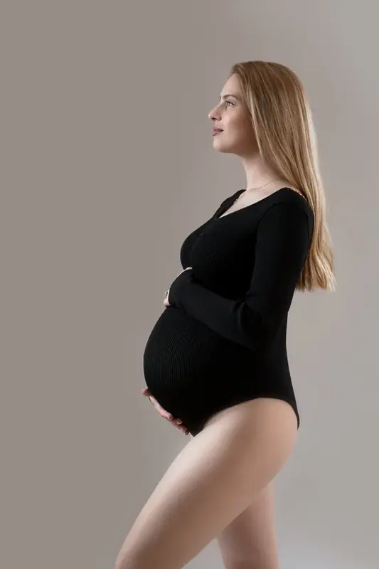 Expectant mother in a black bodysuit standing in profile against a grey backdrop
