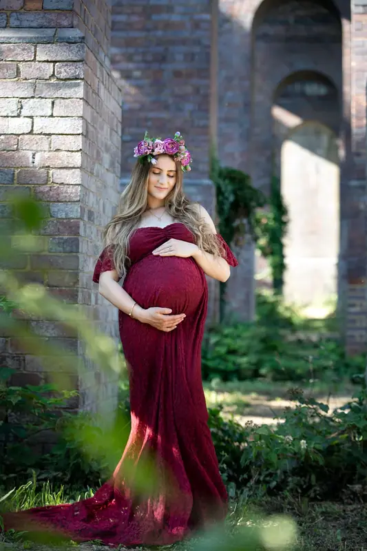 Expectant mother in a burgundy gown and flower crown in a brick archway