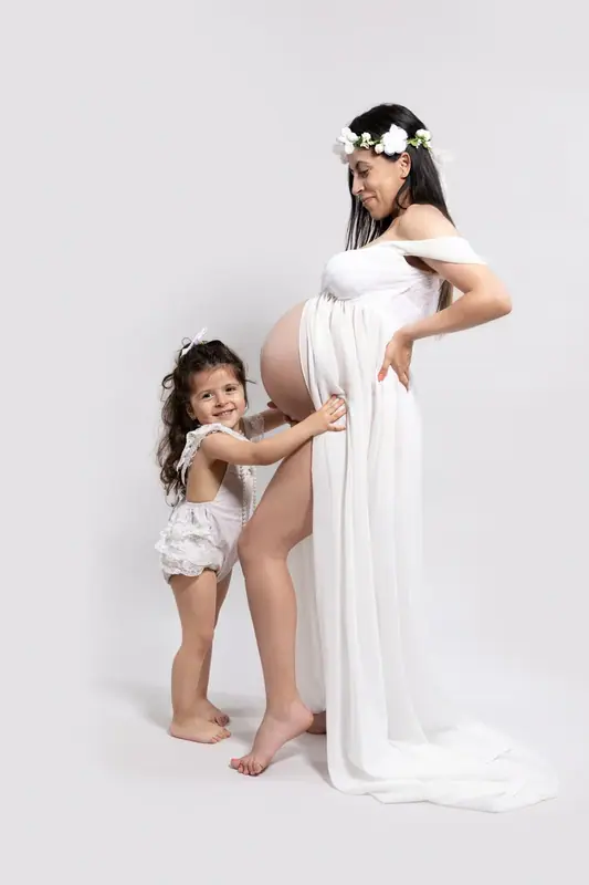 Expectant mother in a white gown with her young daughter, white studio