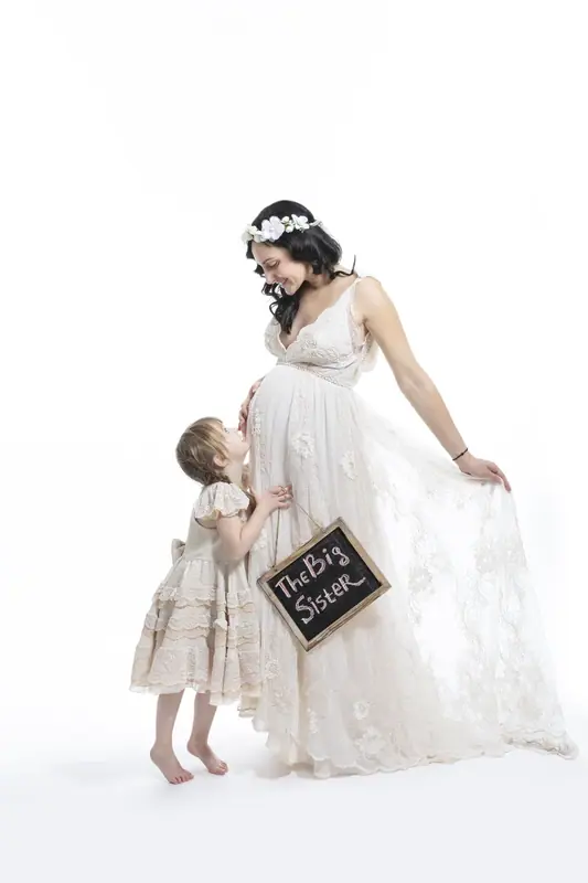 Expectant mother in a white gown with a small child holding a chalkboard sign