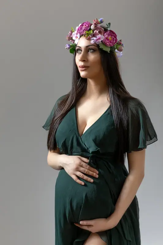 Expectant mother in a dark green dress and flower crown, white studio
