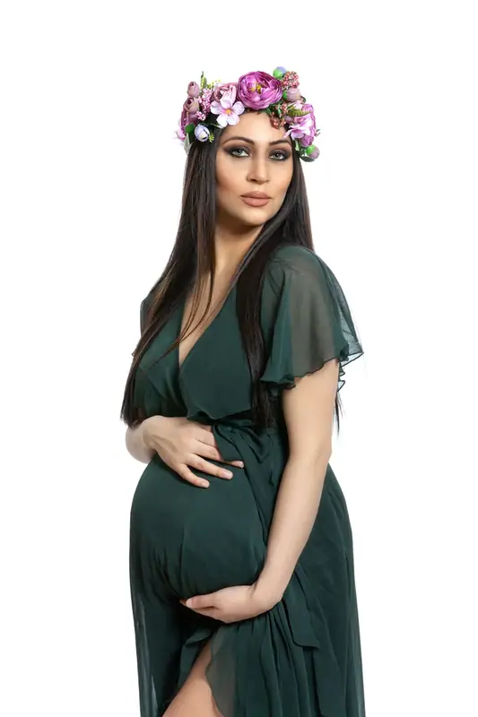 Expectant mother in a dark green dress with a hand on her bump, white studio