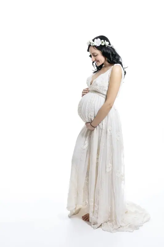 Expectant mother in a white gown and flower crown, white studio