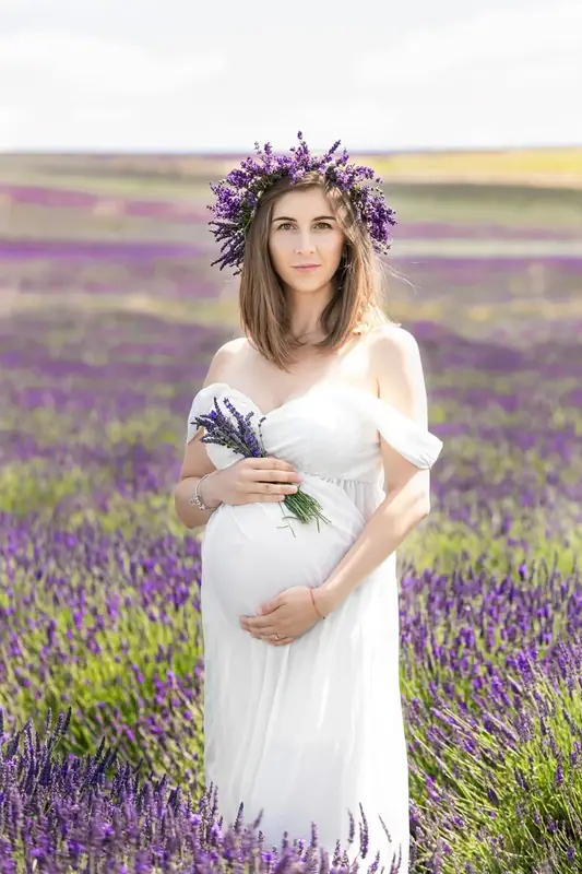 Expectant mother in a white dress and flower crown holding lavender in a lavender field