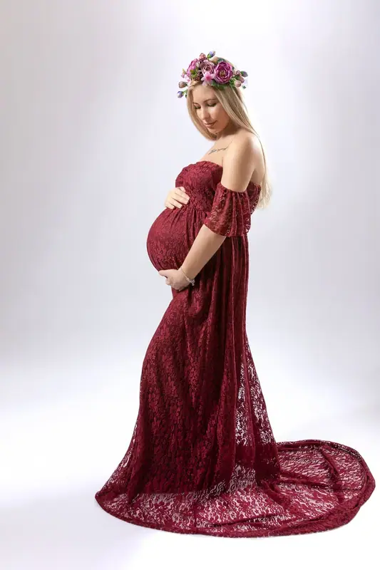 Expectant mother in a long burgundy lace gown, white studio