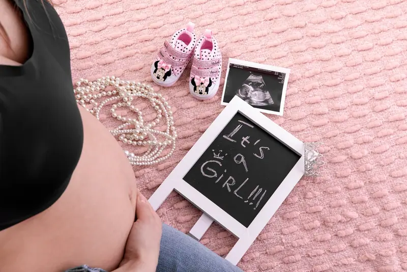 Close-up of hands holding baby shoes, pearls and a small chalkboard sign on a pink blanket