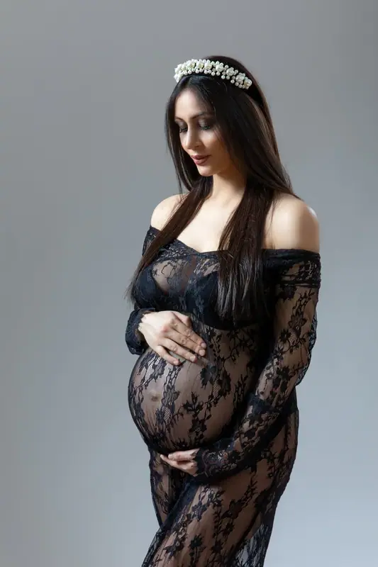 Expectant mother in a black lace gown and flower crown against a grey backdrop