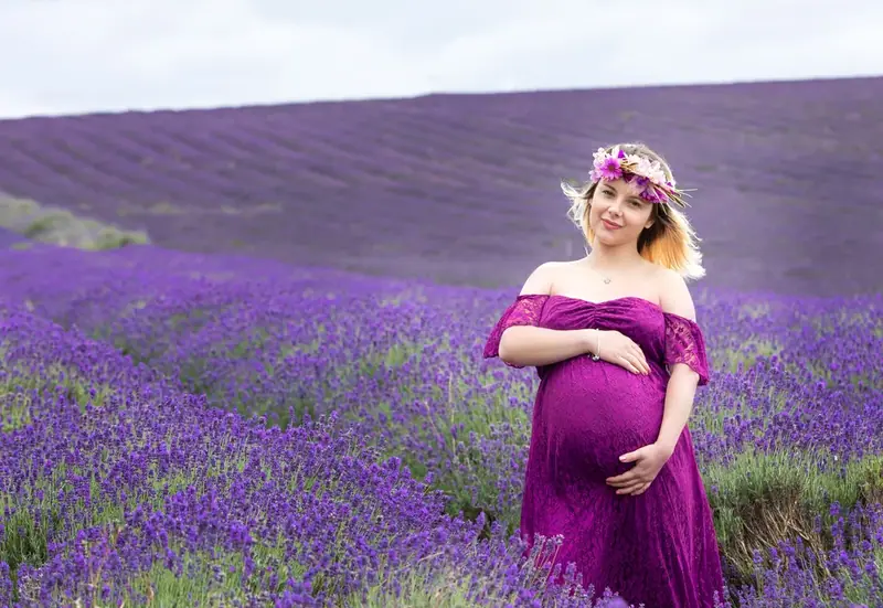 Expectant mother in a purple gown and flower crown standing in a lavender field