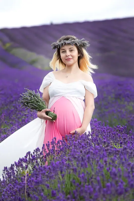 Expectant mother in a pink and white outfit sitting among rows of lavender