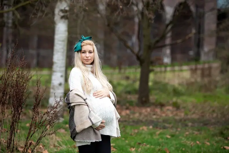 Expectant mother in a flower headband standing among trees