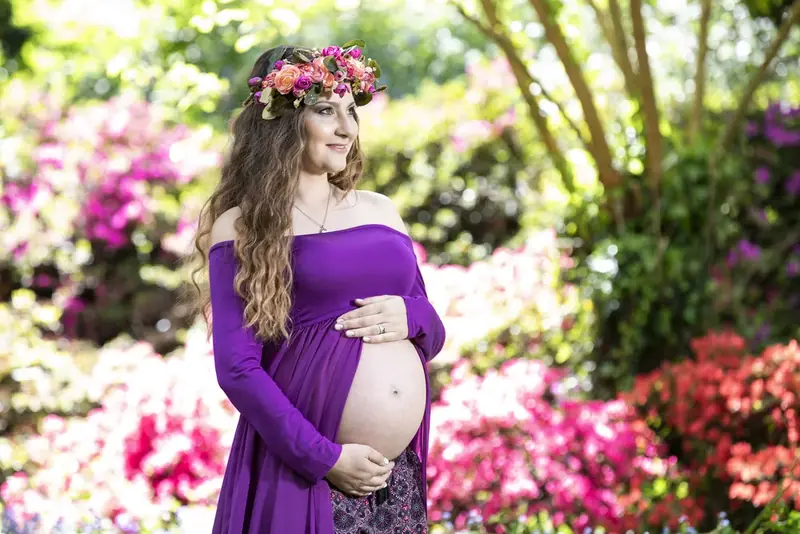 Expectant mother in a purple dress and flower crown among flowering shrubs