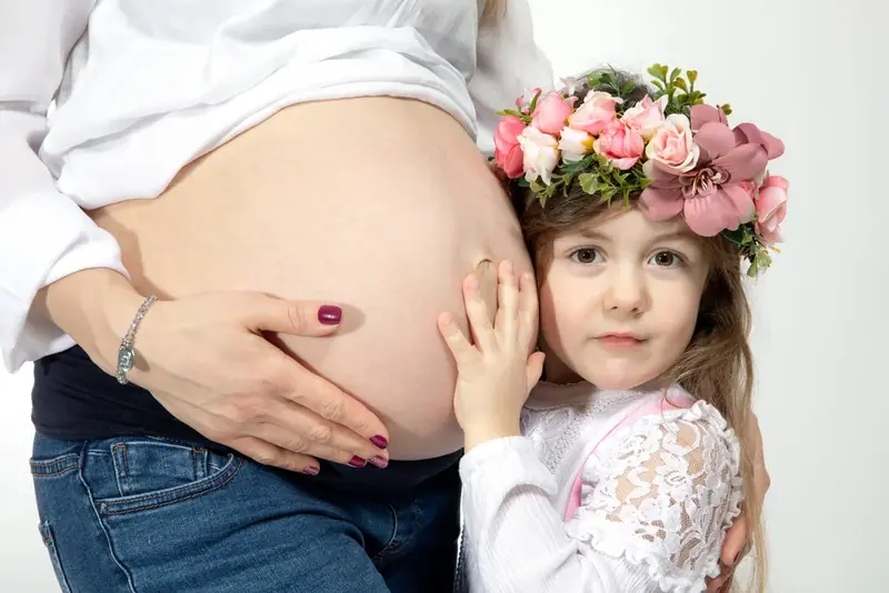 Young girl in a flower crown resting her hands on her mother's bare bump