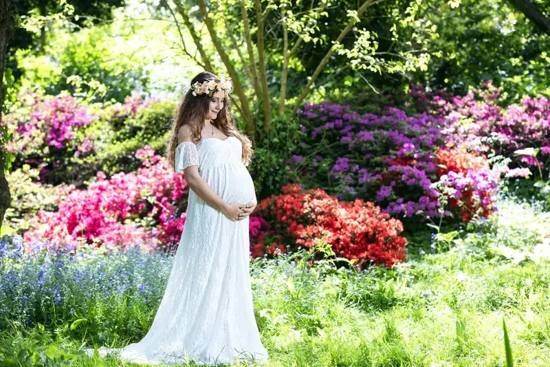 Expectant mother in white standing among colourful flowering shrubs