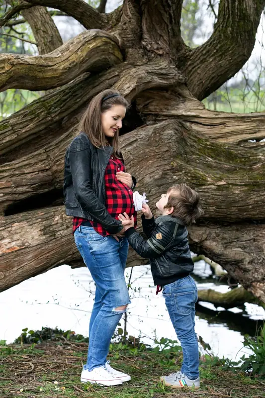 Expectant mother in a checked shirt standing beneath a large old tree