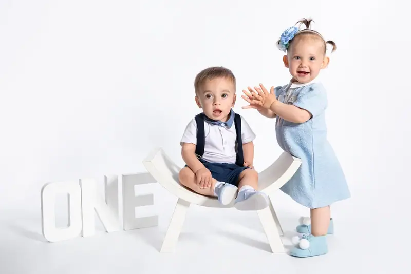 Two babies in blue sitting on a small white bench beside the word ONE