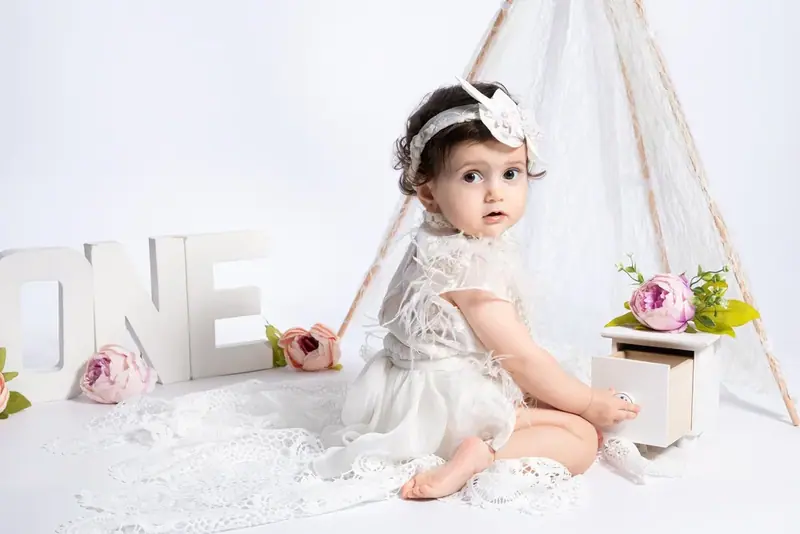 Baby in a white dress sitting under a teepee with the word ONE