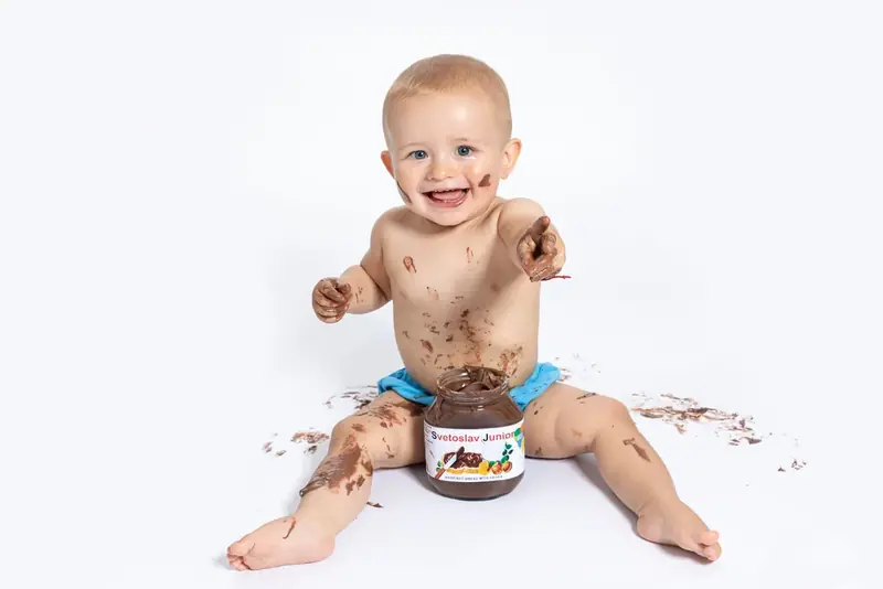 Baby sitting on a white backdrop with chocolate spread on their face and hands