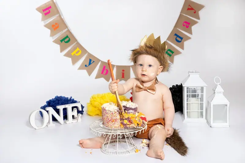 Baby with a birthday cake, a bunting banner and the word ONE