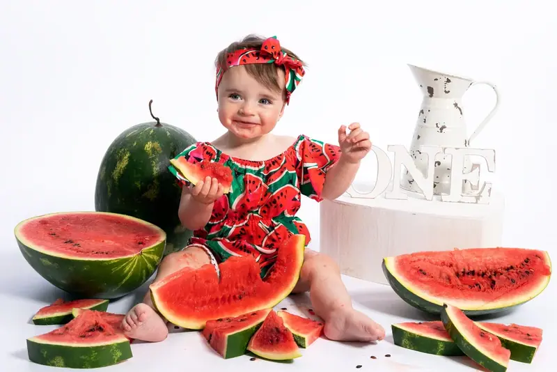 Baby with a red headband sitting among slices of watermelon