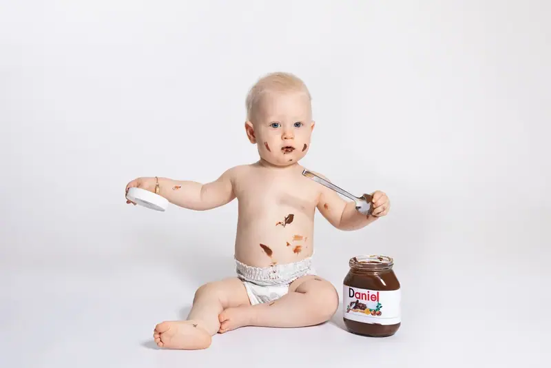 Baby sitting on a white backdrop with a jar of chocolate spread