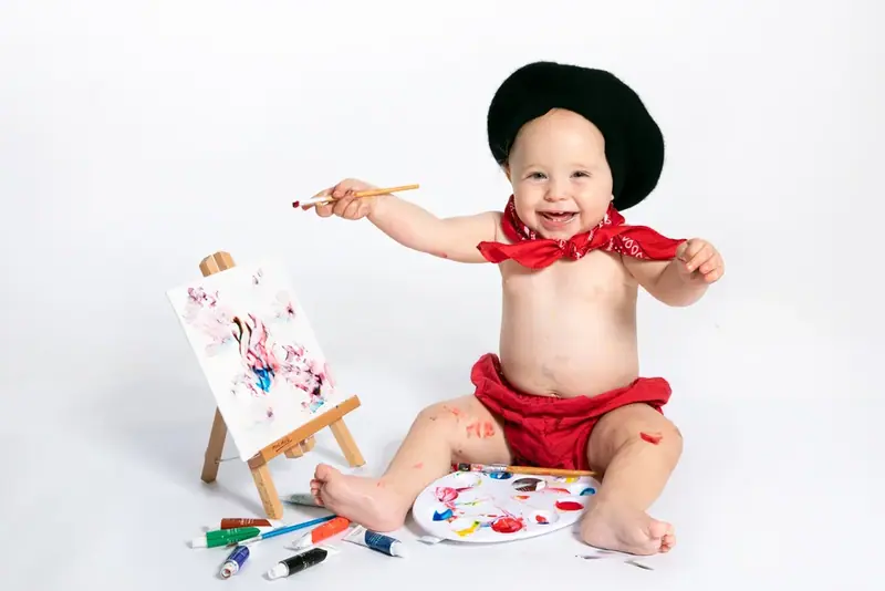 Baby in a black beret and red neckerchief painting at a small easel