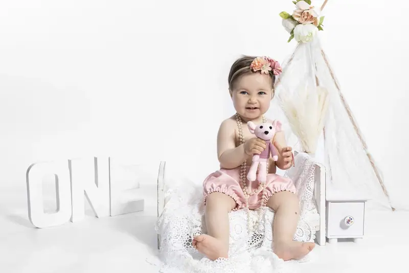 Baby in a pink outfit sitting beside a teepee and the word ONE