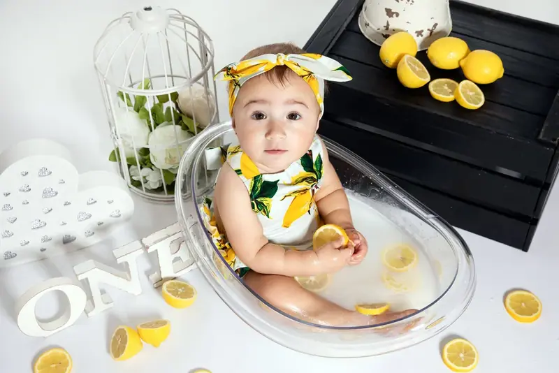 Baby with a lemon-print headband sitting in a bowl of milk with lemon slices