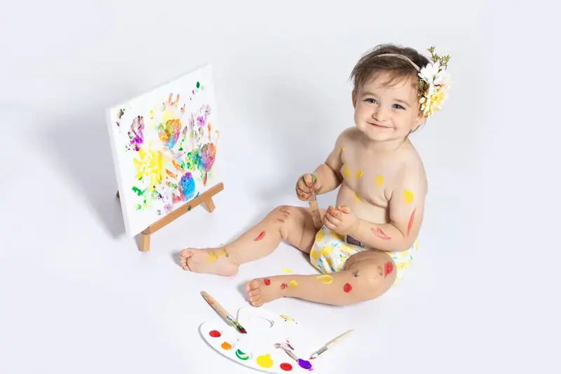 Baby sitting beside a small easel and a colourful painting