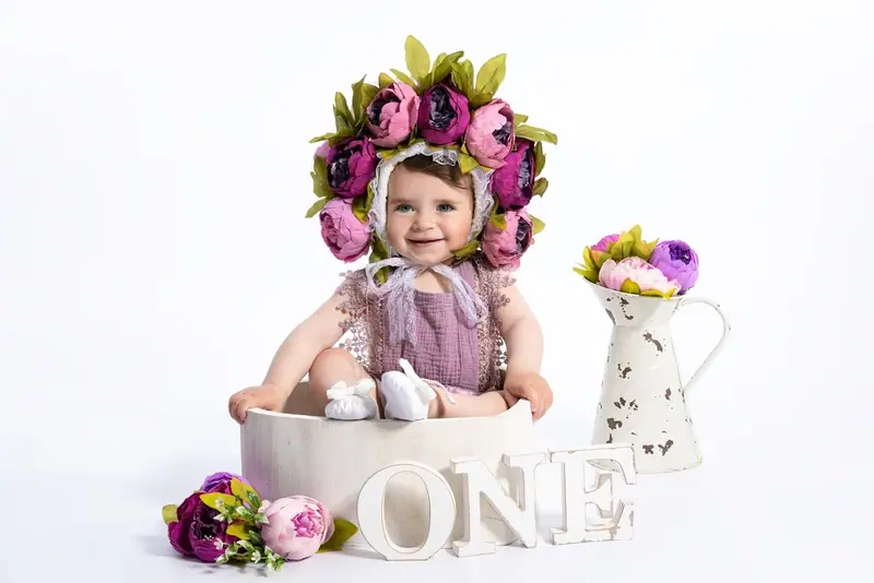 Baby wearing a purple flower crown sitting in a bowl beside the word ONE