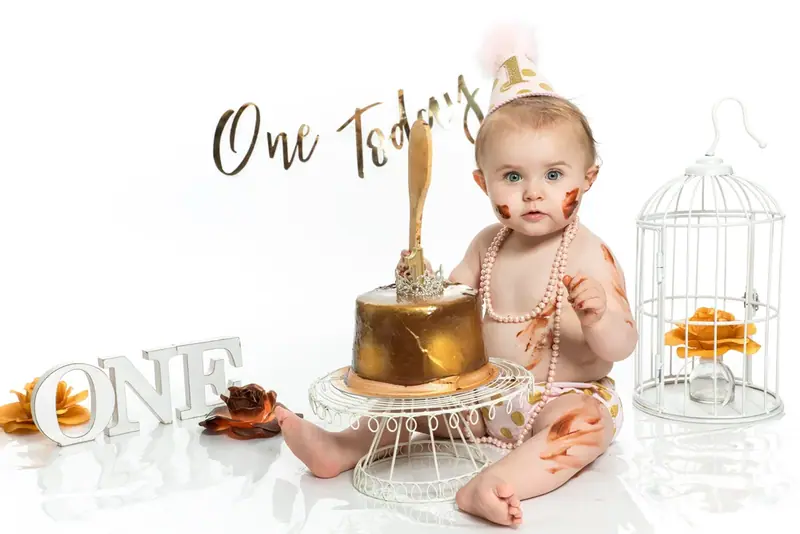 Baby beside a gold birthday cake with a One Today sign and the word ONE
