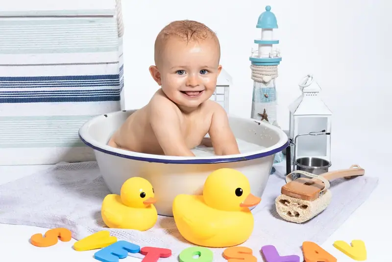 Baby sitting in a small tin bath with yellow rubber ducks