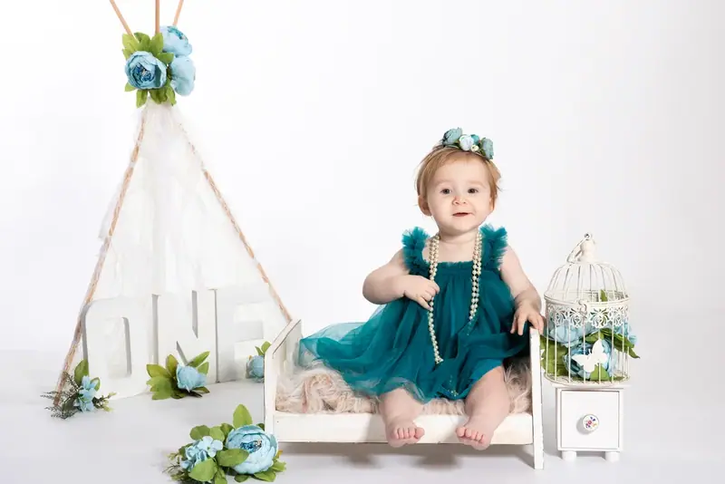 Baby in a teal dress sitting on a small white bench under a teepee