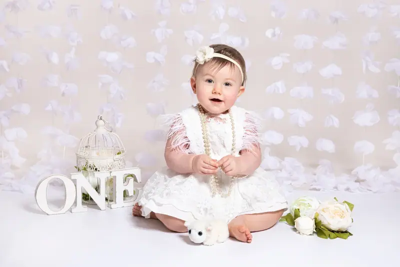 Baby in a white dress and headband sitting beside the word ONE on a fur rug