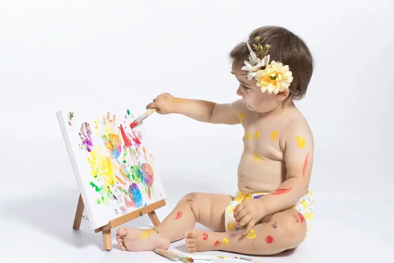 Baby with a flower headband finger-painting on a canvas