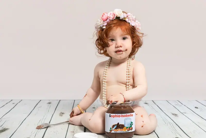 Baby with a flower headband and pearls sitting on a white wooden floor
