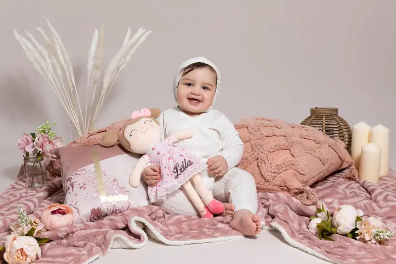 Baby in a bonnet sitting on pink blankets with dried grasses
