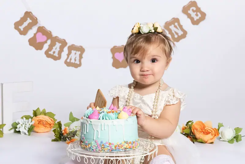 Baby with a small blue birthday cake beneath a bunting banner