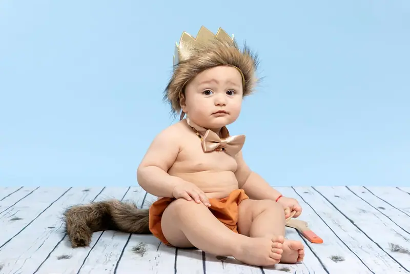 Baby with a crown sitting on a white wooden floor against a blue backdrop