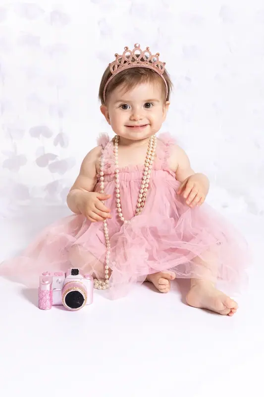Baby in a pink tutu and tiara holding a small camera