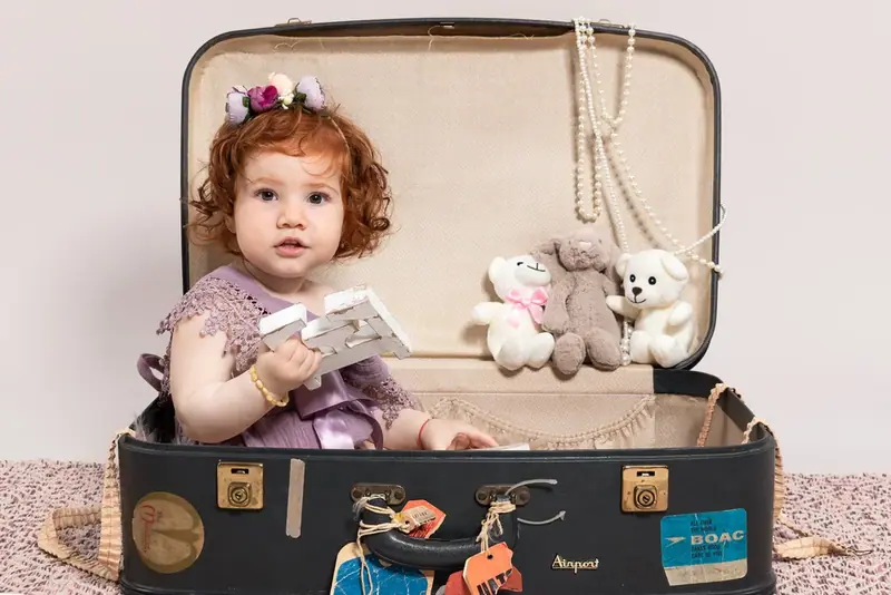 Baby sitting inside an open vintage suitcase with soft toys