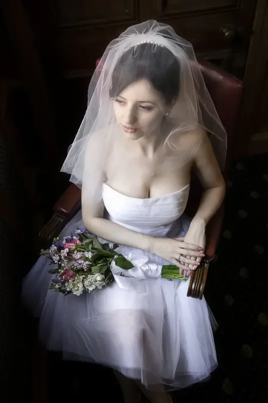 Bride in a short white dress and veil holding a bouquet, seated indoors