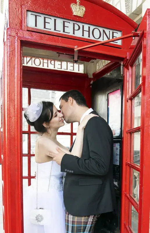 Bride and groom kissing inside a red telephone box